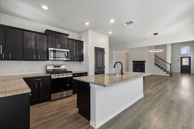 kitchen with hardwood / wood-style floors, pendant lighting, a kitchen island with sink, sink, and stainless steel appliances