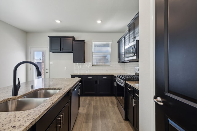 kitchen with light stone countertops, appliances with stainless steel finishes, tasteful backsplash, sink, and wood-type flooring