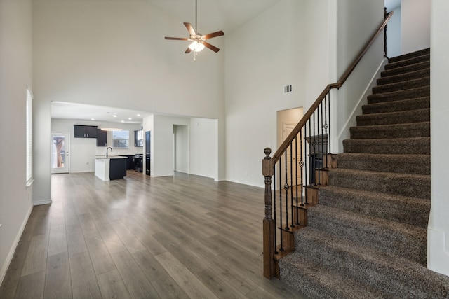 unfurnished living room with a high ceiling, ceiling fan, dark wood-type flooring, and sink