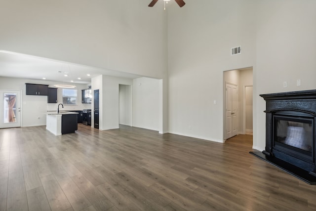 unfurnished living room featuring ceiling fan, dark hardwood / wood-style flooring, sink, and a high ceiling