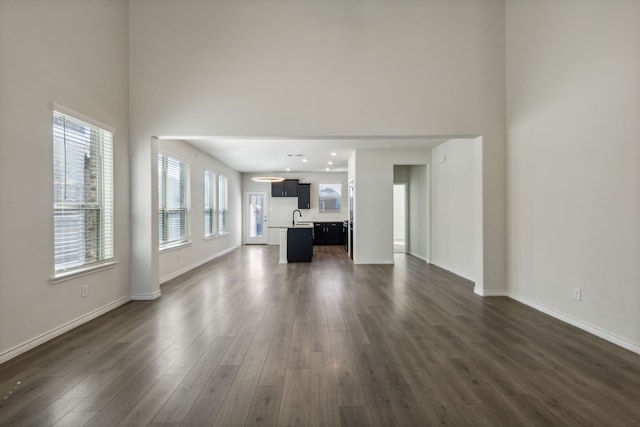 unfurnished living room with a high ceiling, a wealth of natural light, dark wood-type flooring, and sink