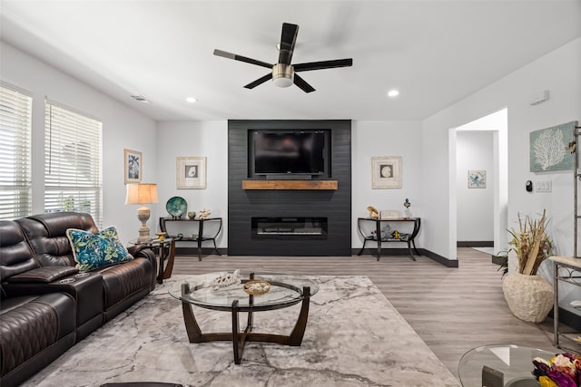 living room with ceiling fan, a fireplace, and light hardwood / wood-style floors