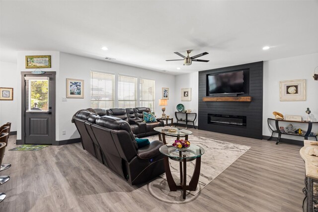 living room with ceiling fan, a large fireplace, and light hardwood / wood-style flooring