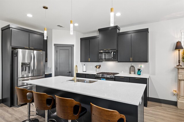 kitchen with pendant lighting, a center island with sink, sink, light hardwood / wood-style flooring, and appliances with stainless steel finishes