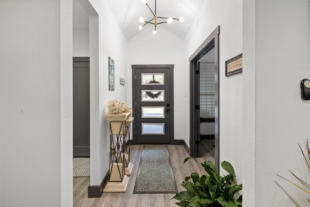 foyer entrance featuring an inviting chandelier, light wood-type flooring, and vaulted ceiling