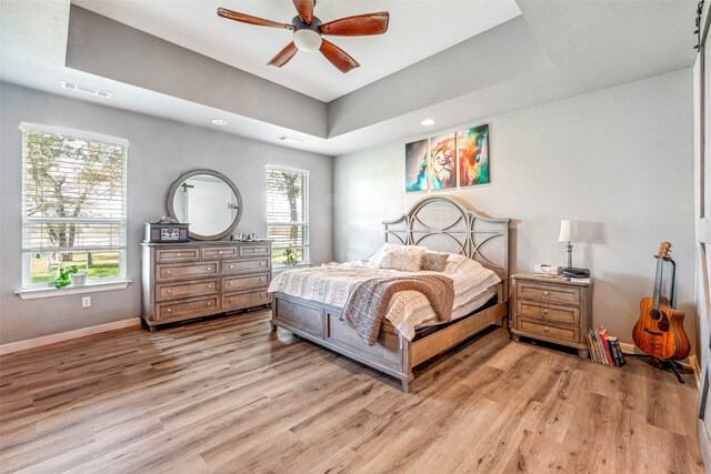 bedroom with ceiling fan, a raised ceiling, and light hardwood / wood-style flooring