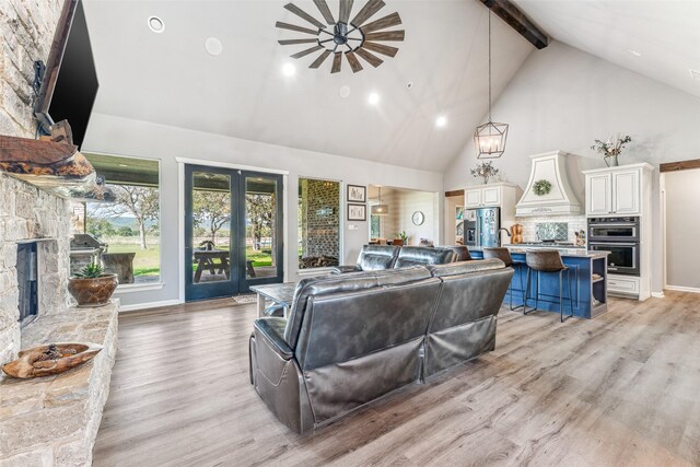 living room featuring beam ceiling, ceiling fan, high vaulted ceiling, a fireplace, and light wood-type flooring