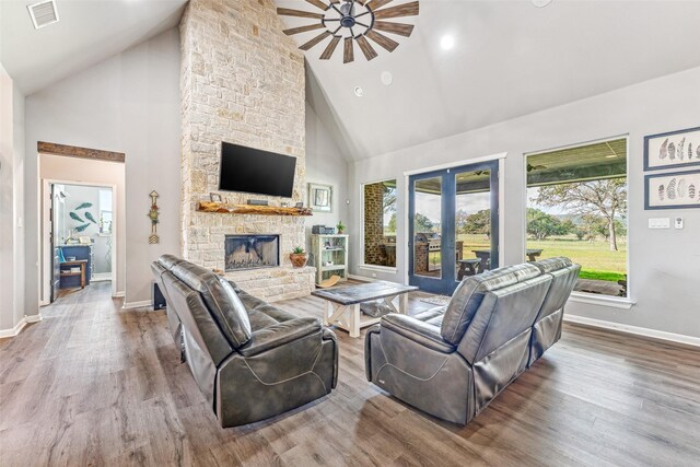 living room featuring hardwood / wood-style floors, ceiling fan, a stone fireplace, and high vaulted ceiling