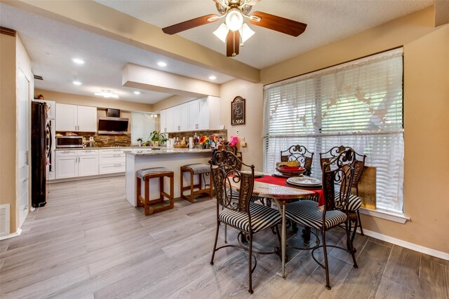 dining area with a textured ceiling, light wood-type flooring, and ceiling fan