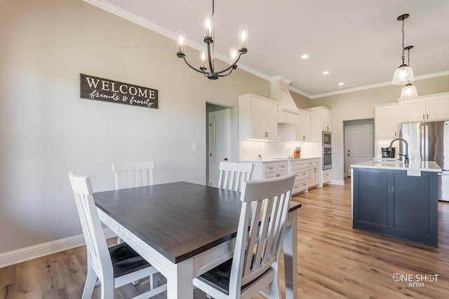 dining room with a chandelier, light wood-type flooring, crown molding, and sink