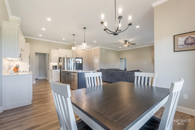 dining area with light wood-type flooring, ceiling fan with notable chandelier, crown molding, and sink