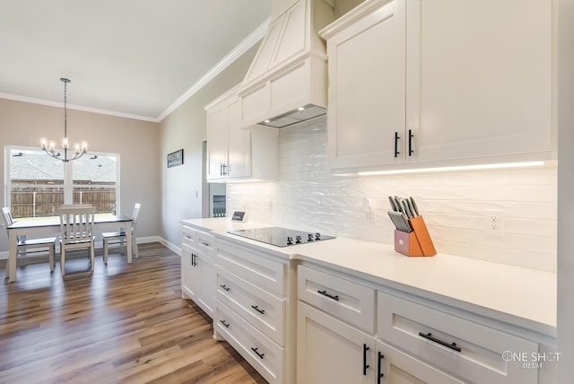 kitchen with premium range hood, white cabinets, black electric cooktop, ornamental molding, and a notable chandelier