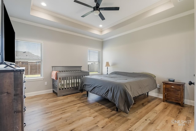 bedroom with ceiling fan, crown molding, light hardwood / wood-style flooring, and a tray ceiling