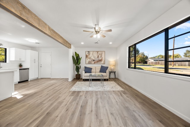 unfurnished room with beamed ceiling, light wood-type flooring, ceiling fan, and a healthy amount of sunlight