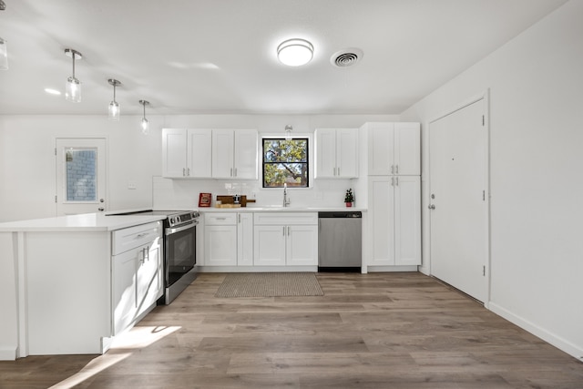 kitchen featuring white cabinetry, stainless steel appliances, kitchen peninsula, pendant lighting, and light wood-type flooring