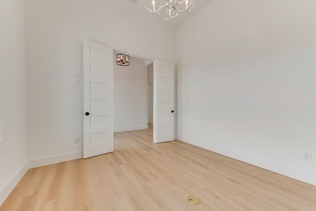 empty room with light wood-style flooring, a chandelier, and baseboards