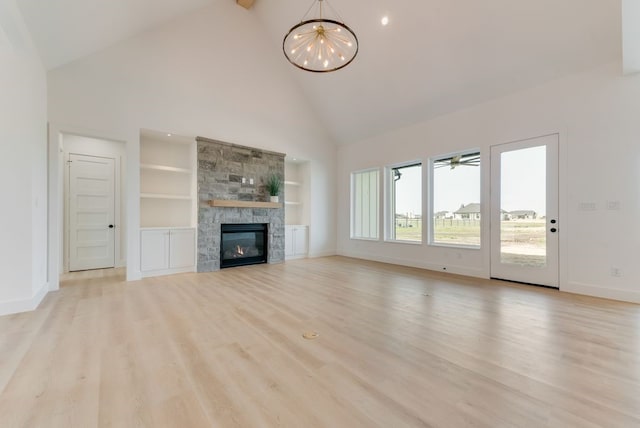 unfurnished living room with high vaulted ceiling, built in shelves, a stone fireplace, light wood-style flooring, and baseboards