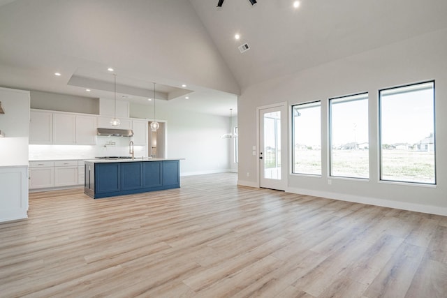 unfurnished living room featuring ceiling fan, a towering ceiling, and light hardwood / wood-style floors