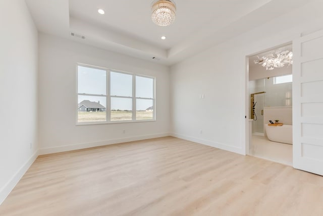 unfurnished bedroom featuring a tray ceiling, a notable chandelier, light wood finished floors, visible vents, and baseboards