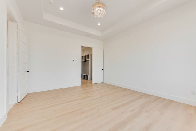 unfurnished room with light wood finished floors, recessed lighting, a raised ceiling, and baseboards