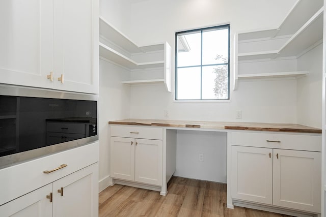 kitchen featuring black microwave, white cabinetry, butcher block counters, and light hardwood / wood-style flooring