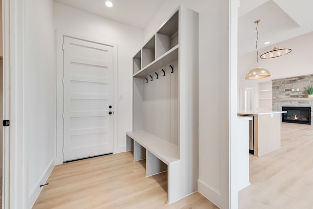 mudroom featuring light wood-style floors, recessed lighting, a large fireplace, and built in shelves