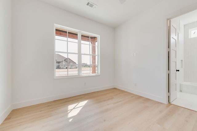 spare room with light wood-type flooring, visible vents, and baseboards