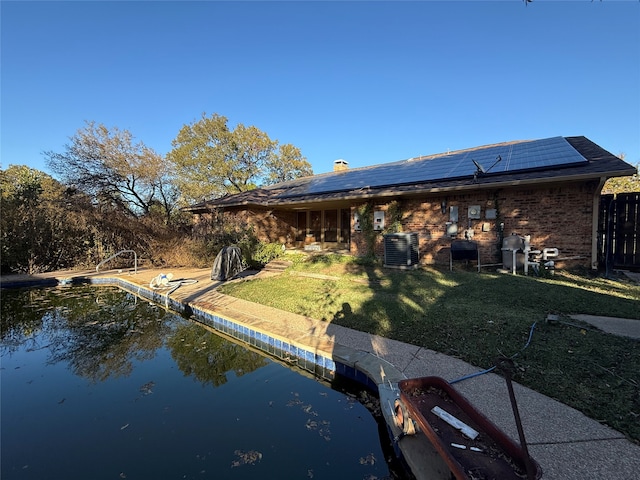 rear view of property with solar panels, a water view, central air condition unit, a lawn, and brick siding