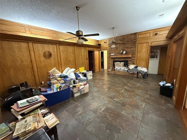 unfurnished living room with a textured ceiling, a brick fireplace, ceiling fan, and wooden walls