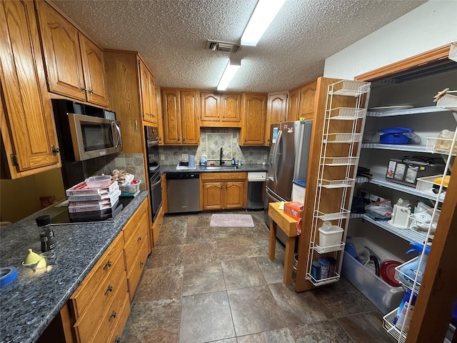 kitchen with backsplash, sink, dark stone countertops, a textured ceiling, and stainless steel appliances