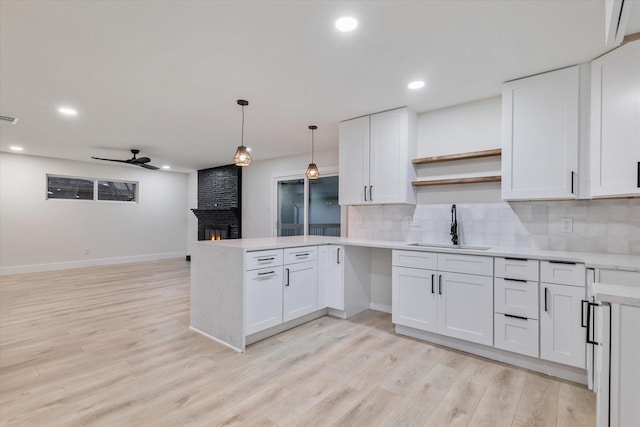 kitchen with kitchen peninsula, a brick fireplace, ceiling fan, sink, and white cabinets