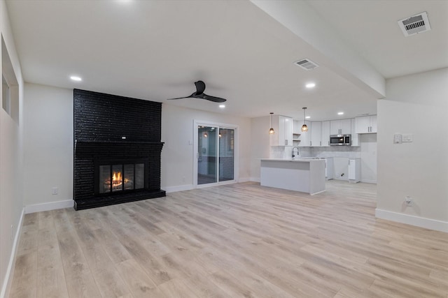 unfurnished living room with a brick fireplace, ceiling fan, sink, and light wood-type flooring