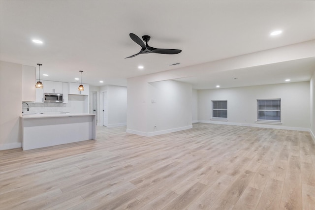 unfurnished living room featuring ceiling fan, sink, and light hardwood / wood-style floors