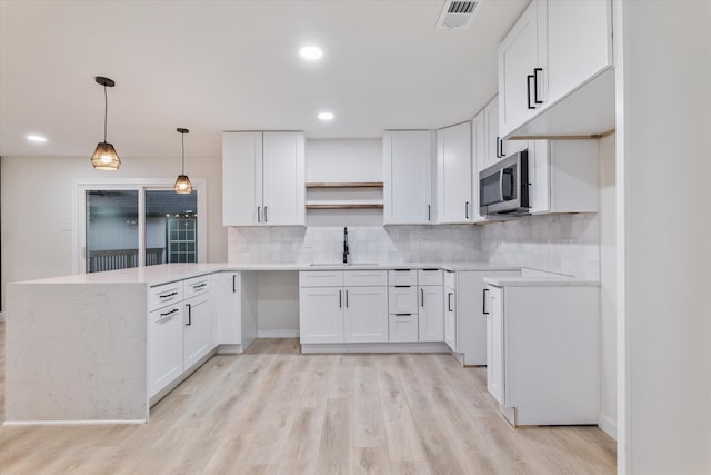 kitchen featuring white cabinetry, sink, light hardwood / wood-style flooring, kitchen peninsula, and decorative backsplash