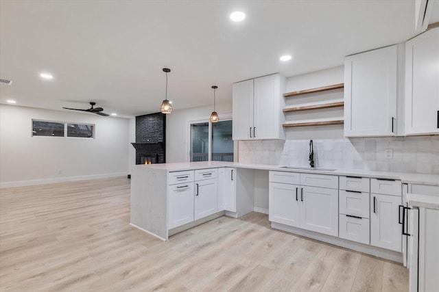 kitchen featuring white cabinets, ceiling fan, sink, and a brick fireplace