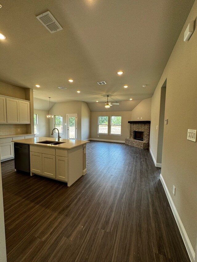 kitchen with ceiling fan with notable chandelier, sink, black dishwasher, white cabinetry, and an island with sink