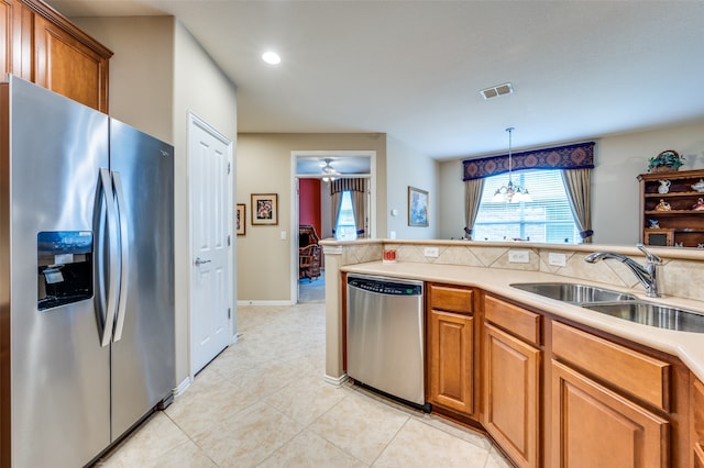 kitchen with sink, stainless steel appliances, pendant lighting, light tile patterned floors, and ceiling fan with notable chandelier