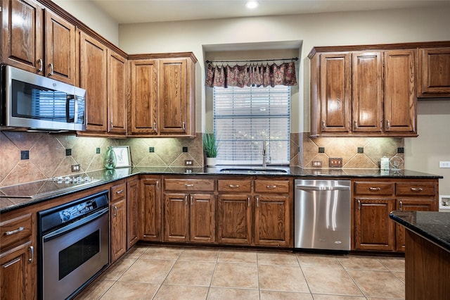 kitchen featuring sink, tasteful backsplash, dark stone countertops, light tile patterned floors, and appliances with stainless steel finishes