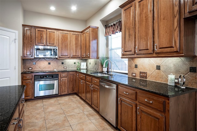 kitchen featuring backsplash, stainless steel appliances, sink, dark stone countertops, and light tile patterned flooring