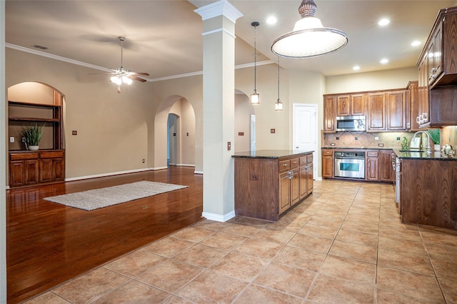 kitchen featuring ornate columns, ceiling fan, stainless steel appliances, crown molding, and decorative backsplash