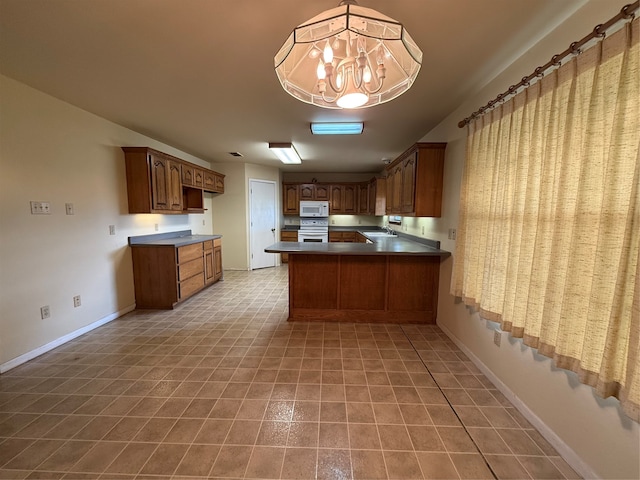 kitchen with kitchen peninsula, white appliances, sink, pendant lighting, and an inviting chandelier