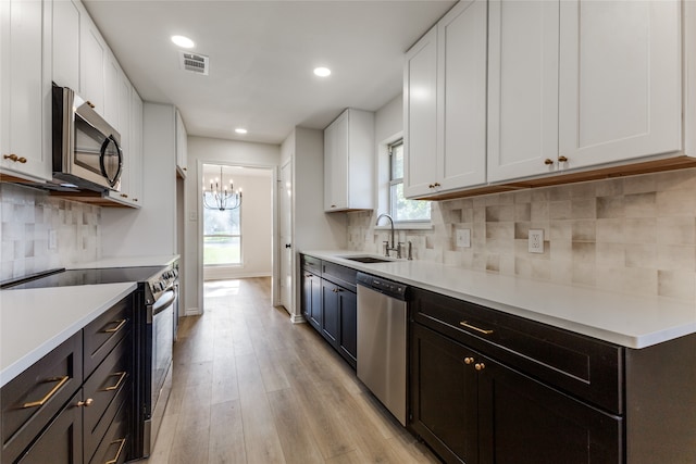 kitchen featuring sink, white cabinetry, an inviting chandelier, stainless steel appliances, and light hardwood / wood-style floors