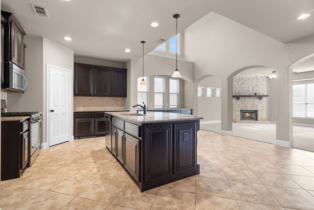 kitchen with ceiling fan, sink, hanging light fixtures, stainless steel appliances, and a stone fireplace