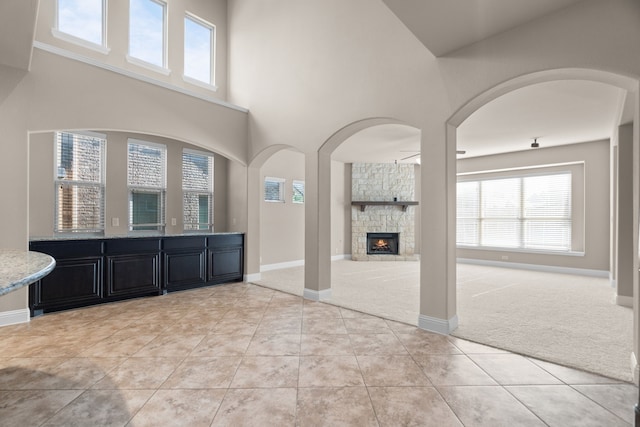 unfurnished living room featuring ceiling fan, a stone fireplace, a towering ceiling, and light carpet