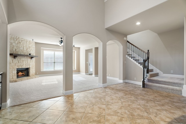 carpeted entryway with ceiling fan and a stone fireplace