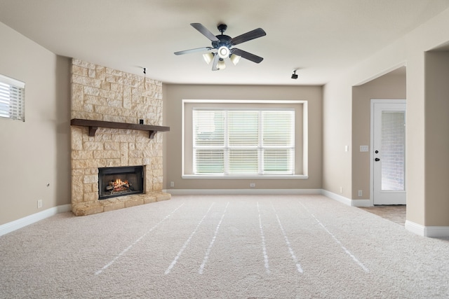 unfurnished living room featuring ceiling fan, a stone fireplace, and light carpet