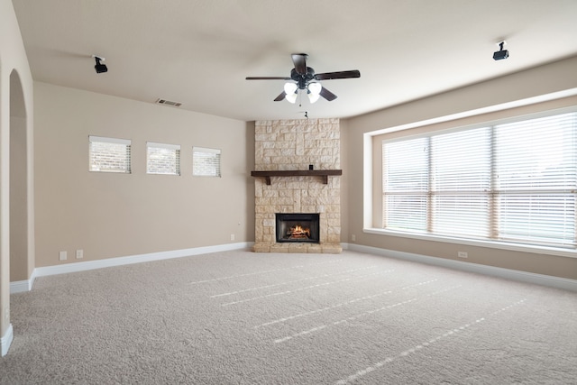 unfurnished living room with a stone fireplace, ceiling fan, and carpet