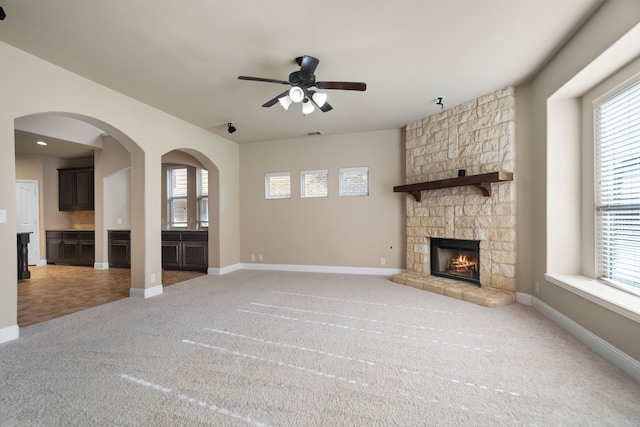 unfurnished living room featuring ceiling fan, a healthy amount of sunlight, carpet floors, and a fireplace