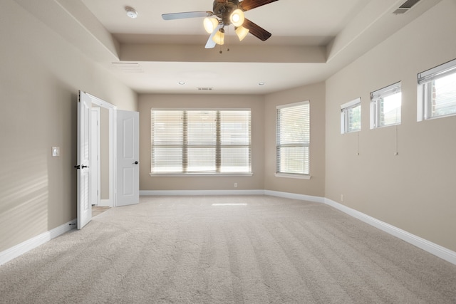 spare room with light carpet, a tray ceiling, and ceiling fan