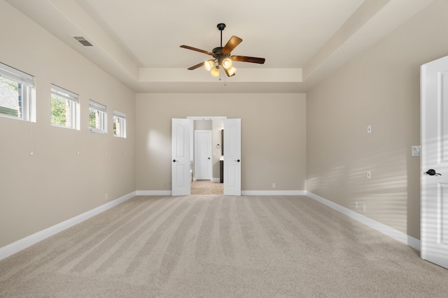 unfurnished room with ceiling fan, a raised ceiling, and light carpet